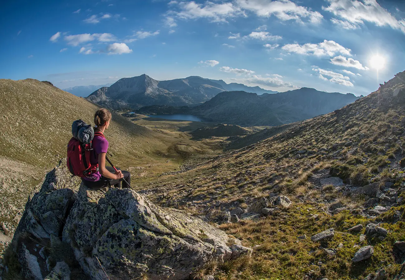 Senderista con mochila en una monta&ntilde;a, valle y nubes bajo el sol