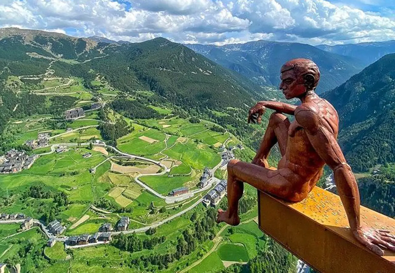 Estatua humana sobre mirador, vista de valles verdes y monta&ntilde;as al fondo.