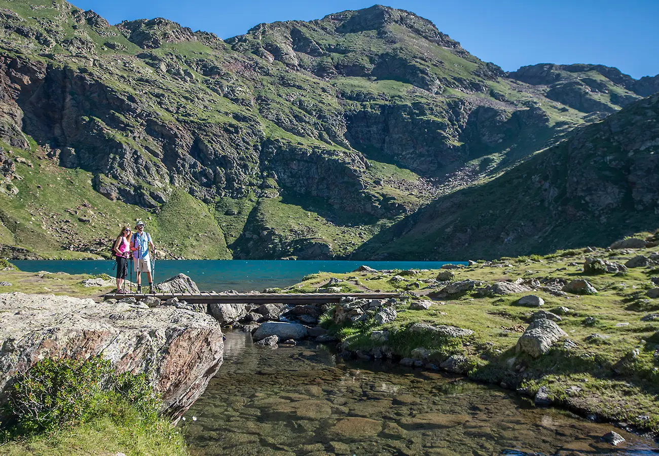 Senderistas con mochila sobre un puente frente a un lago y monta&ntilde;as alpinas