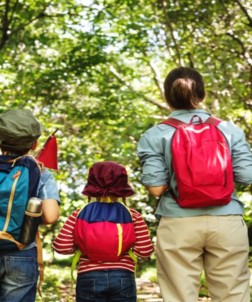 Tres ni&ntilde;os con mochilas caminan por un sendero entre &aacute;rboles verdes.