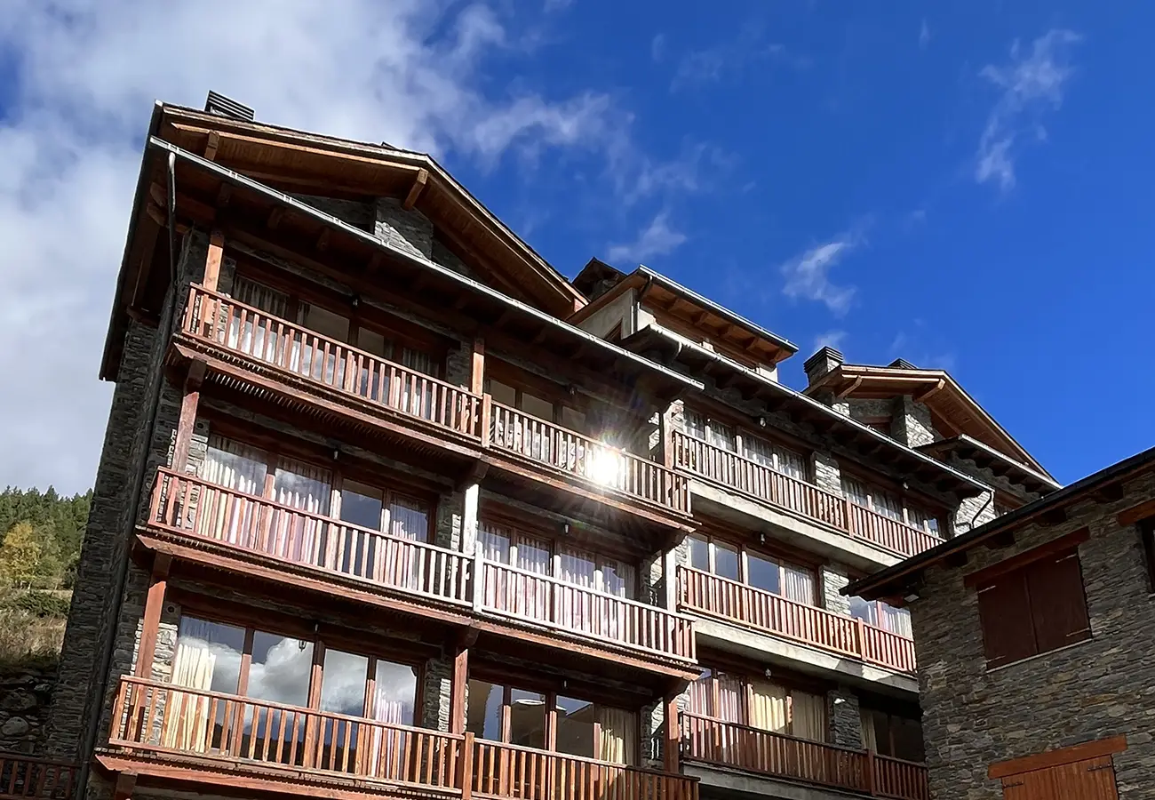 Fachada de casa de madera y piedra con balcones y cielo azul.