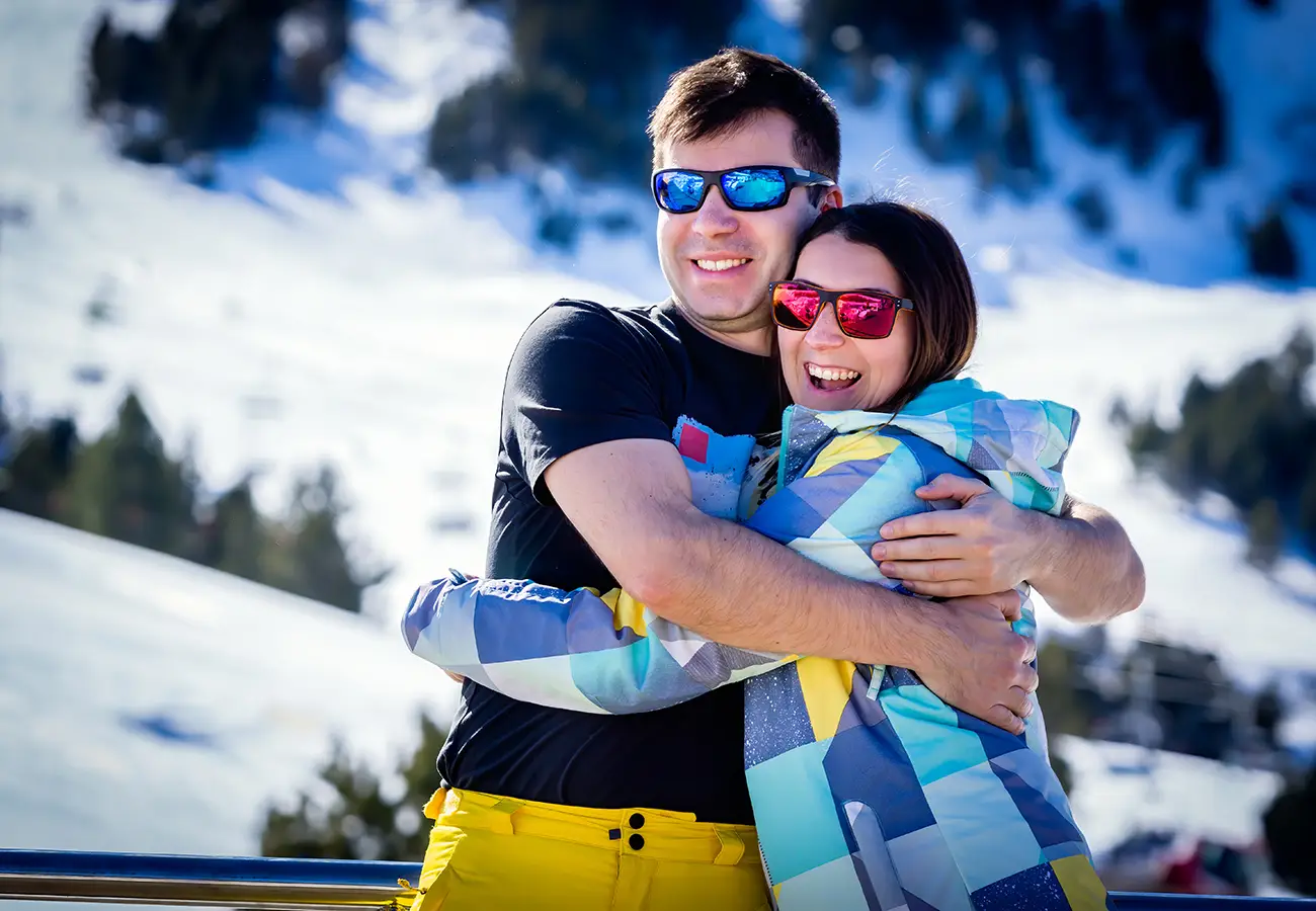 Pareja en la nieve con gafas de sol, abrazados y sonriendo en una monta&ntilde;a