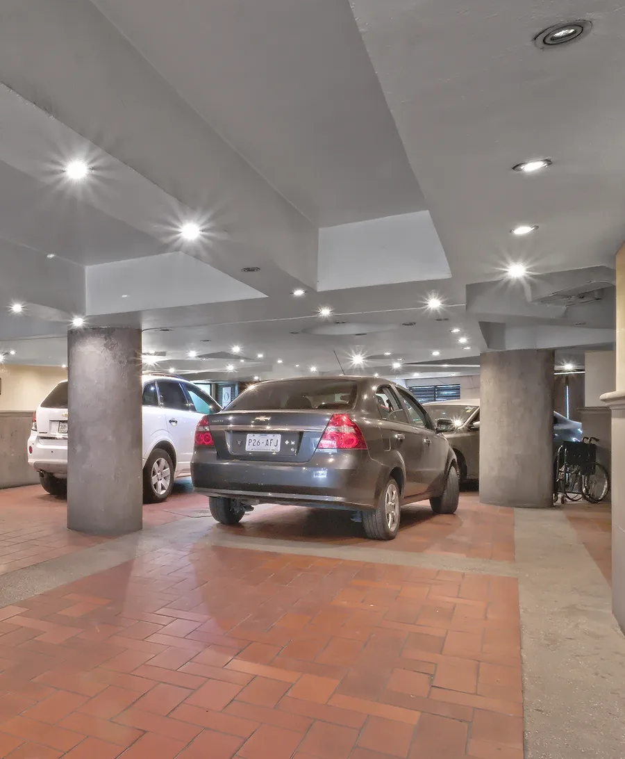 Coches estacionados en un garaje con columnas y luces de techo.