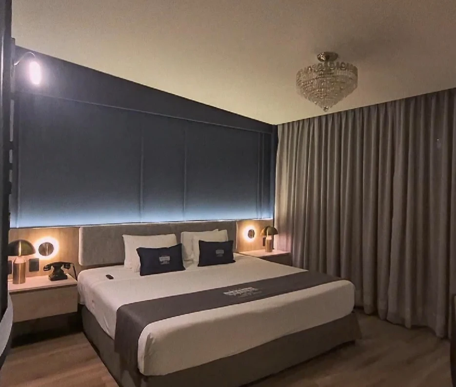 Dormitorio moderno con cama doble, mesas laterales y cortinas beige.