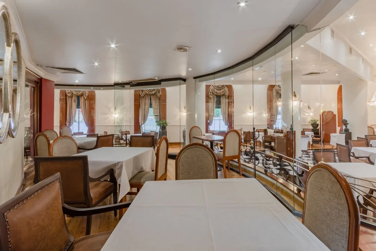 Comedor elegante con mesas, sillas y ventanales de vidrio con cortinas doradas