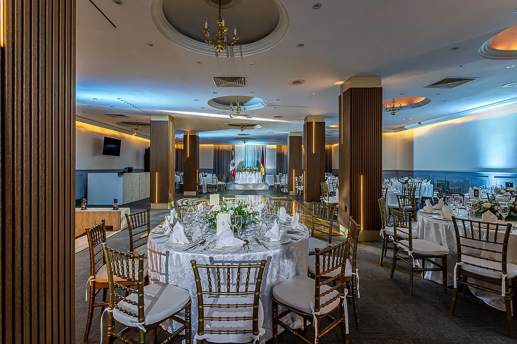 Sala de banquete elegante con mesas cubiertas y sillas doradas, decoraci&oacute;n floral