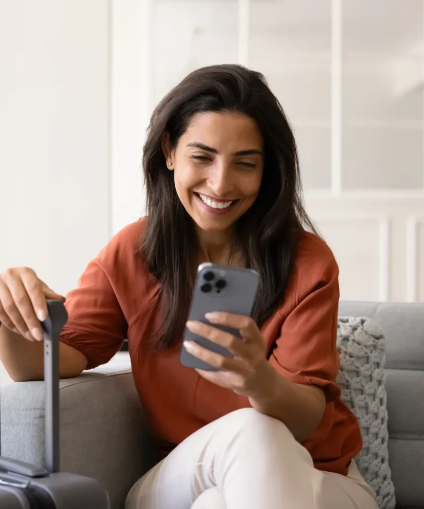 Mujer sonriente en el sof&aacute; usando el celular y una laptop.