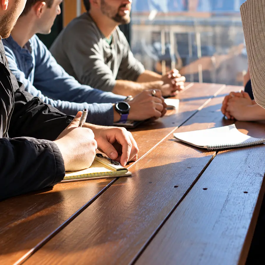 Personas trabajando en una mesa, una persona escribe con l&aacute;piz.
