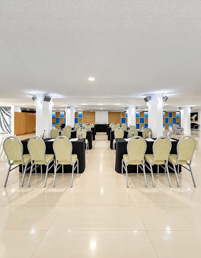 Sala de eventos con mesas y sillas, iluminaci&oacute;n del techo y paredes azules.