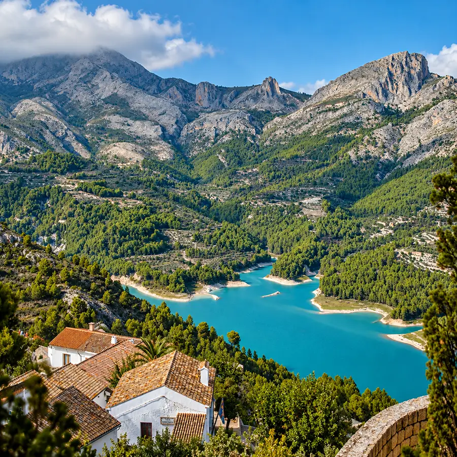 Valle monta&ntilde;oso con r&iacute;o azul y casas blancas, rodeado de bosques y picos