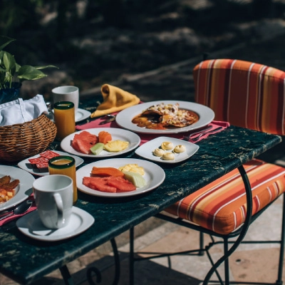 A table set for breakfast outdoors, with fruit and dishes arranged on a green tablecloth.