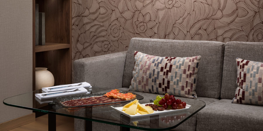 Sof&aacute; gris con cojines, mesa de vidrio con platos de fruta y embutidos.