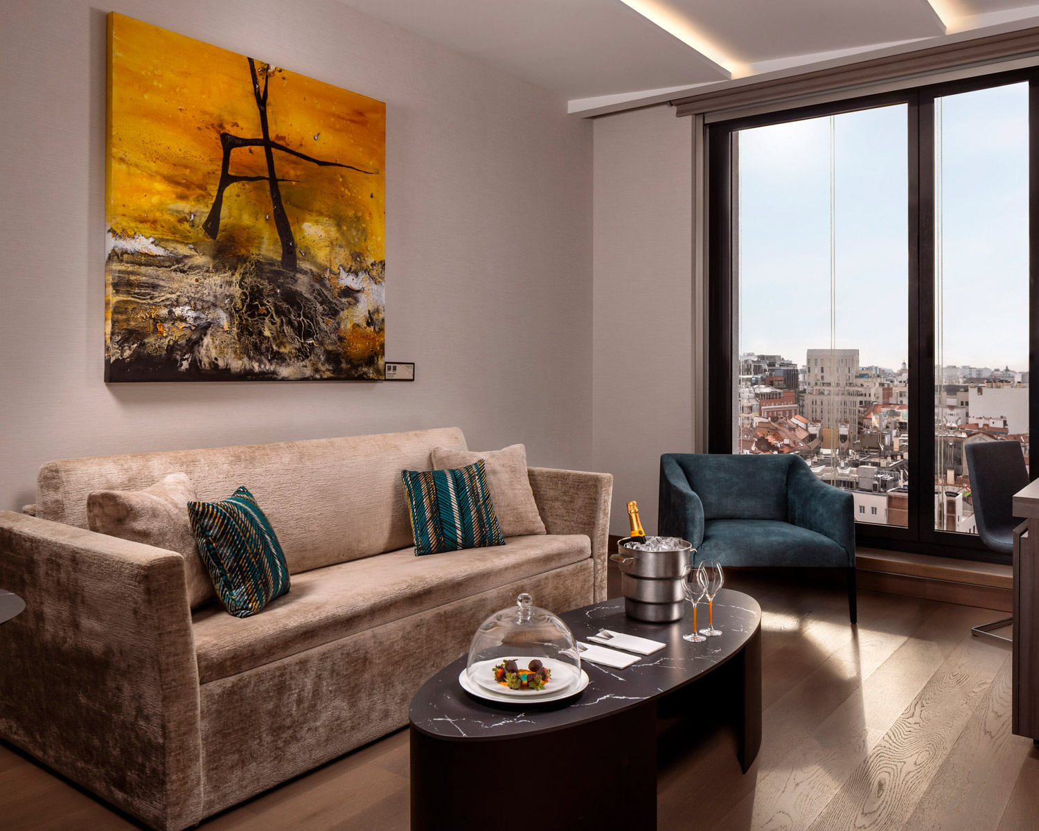 Sala moderna con sof&aacute;, arte abstracto y ventana con vista a la ciudad.