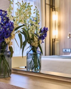Jarr&oacute;n con flores azules y blancas reflejado en un espejo en una habitaci&oacute;n elegante.