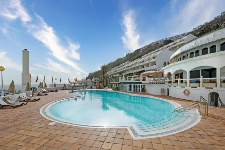 Piscina al aire libre en un hotel con tumbonas y edificios blancos al fondo