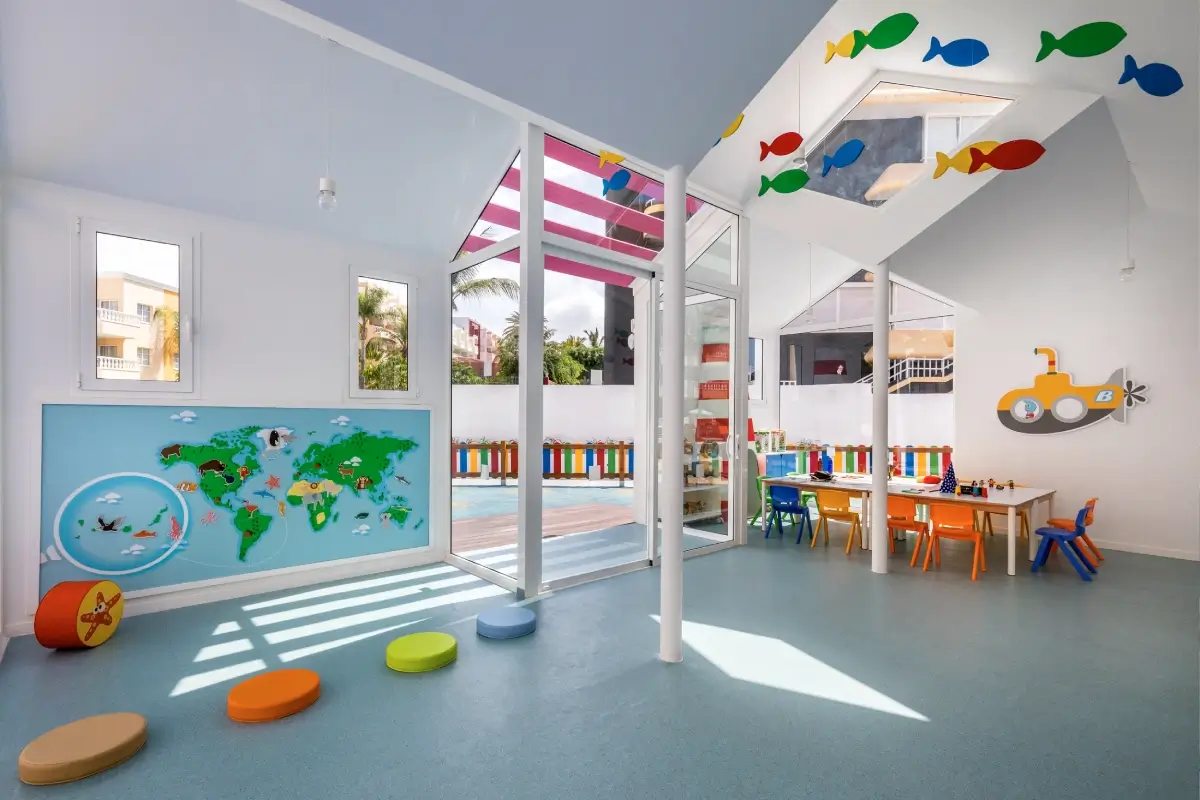 Aula infantil colorida con decoraci&oacute;n de peces y mesas con sillas multicolores.