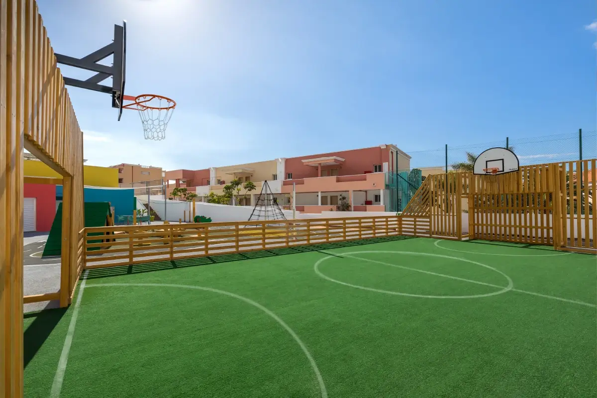 Cancha de b&aacute;squet al aire libre con c&eacute;sped sint&eacute;tico y casas de fondo.
