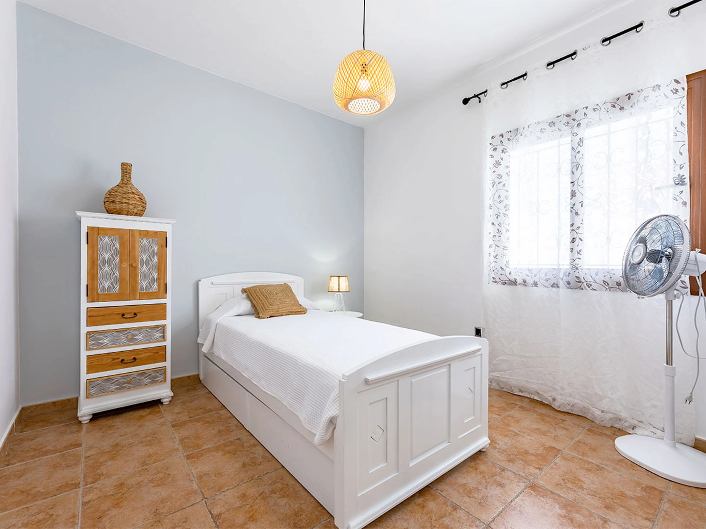 Habitación luminosa con cama, armario y ventilador.