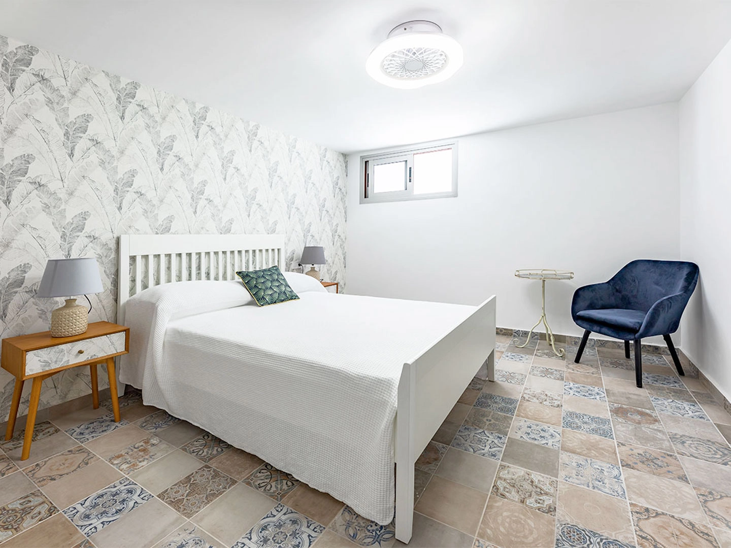 Dormitorio minimalista con cama, silla y papel tapiz de hojas grises.