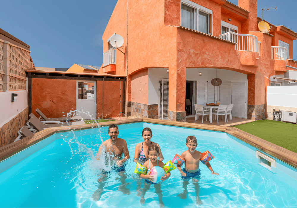 Familia de cuatro personas disfrutando en una piscina frente a una casa naranja.