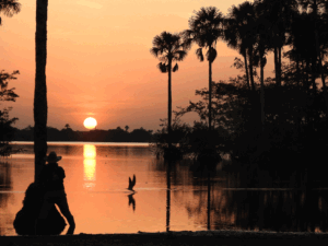 Atardecer sobre una sabana inundable de Casanare, con los colores naranjas del sol reflejados en el agua y la silueta de un llanero.
