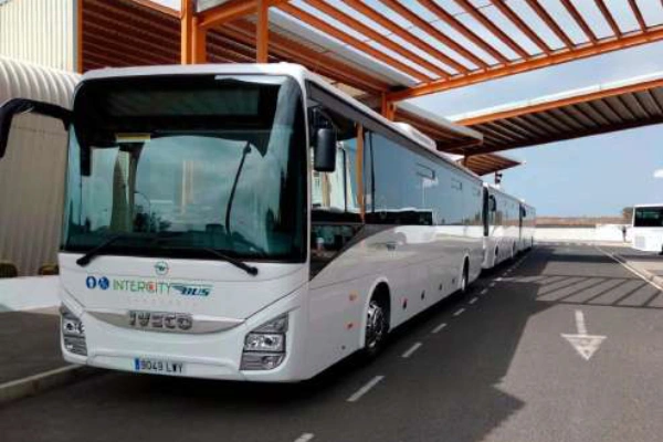 Autobús blanco aparcado en una estación bajo un techo con estructura naranja.