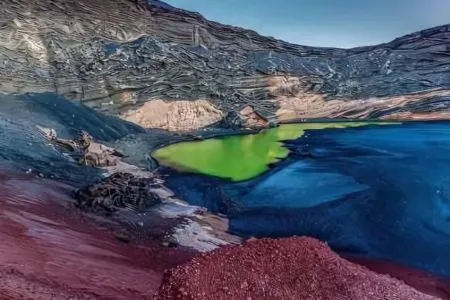 Paisaje colorido con lago verde y formaciones rocosas en tonos rojos y azulados.