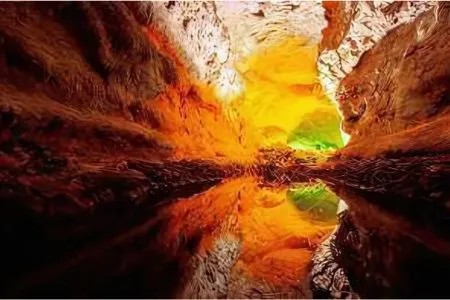 Cueva iluminada en tonos cálidos reflejándose en el agua.