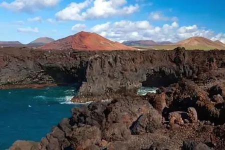 Costa rocosa con montañas al fondo, cielo despejado con nubes esponjosas.