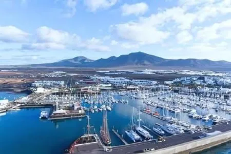 Puerto con barcos y montañas al fondo bajo un cielo azul con nubes.