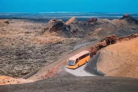 Autobús naranja recorriendo camino en paisaje desértico y rocoso.