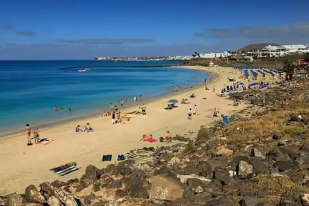 Playa con turistas, sombrillas y mar azul bajo un cielo despejado.