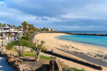 Playa con arena dorada, palmeras y cielo parcialmente nublado.