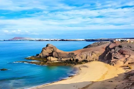 Playa con acantilados, mar azul y cielo despejado con algunas nubes.