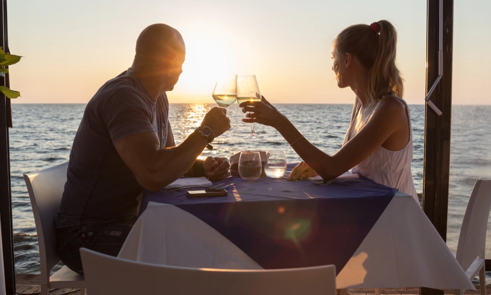 Pareja brindando en una cena junto al mar al atardecer.