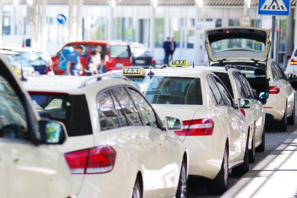 Fila de taxis blancos estacionados en la calle con gente caminando alrededor.