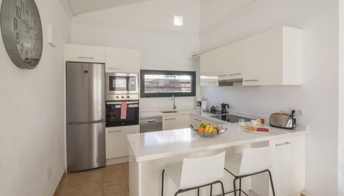 Cocina moderna con electrodomésticos de acero y barra con dos sillas blancas.