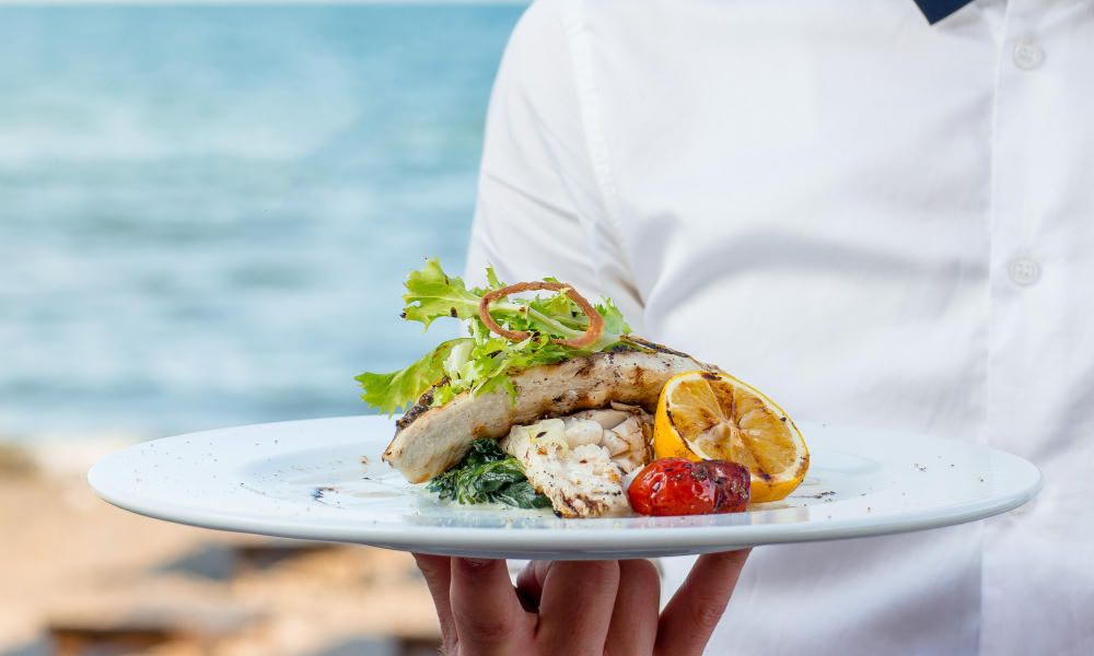 Plato de pescado con guarnición de limón y verduras, servido en la playa.