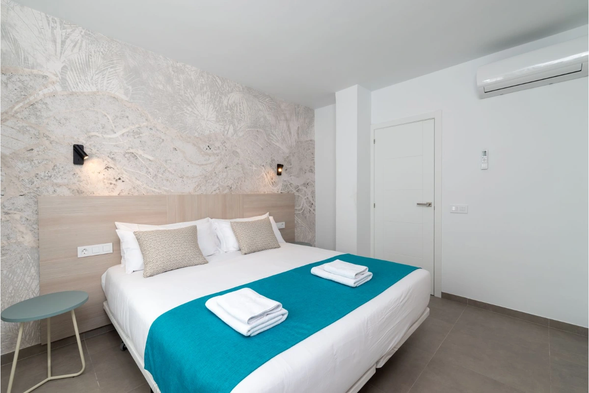 Dormitorio moderno con cama doble, edred&oacute;n turquesa y pared decorativa.