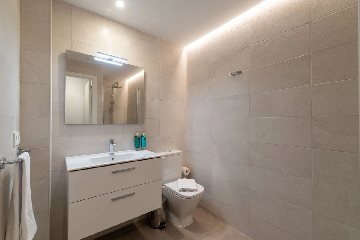 Ba&ntilde;o moderno con lavabo, espejo, inodoro y ducha integrados en dise&ntilde;o minimalista.