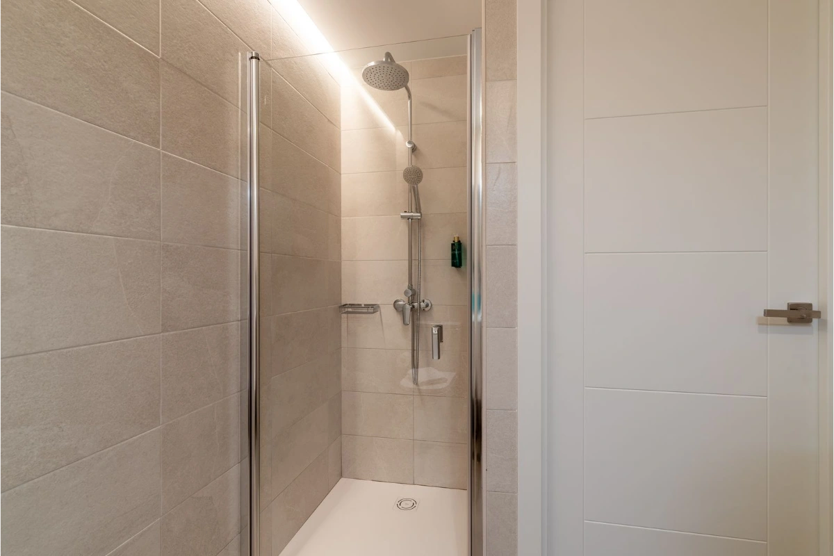 Ducha moderna con azulejos beige y puerta de vidrio.