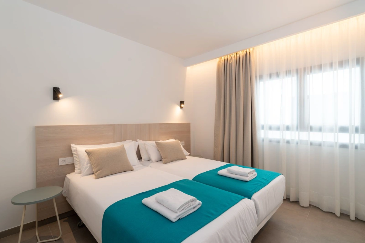 Habitaci&oacute;n de hotel con dos camas individuales y decoraci&oacute;n minimalista.