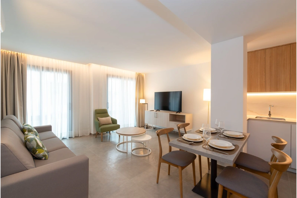 Sala moderna con sof&aacute;, sillas, mesa, TV y cocina integrada.