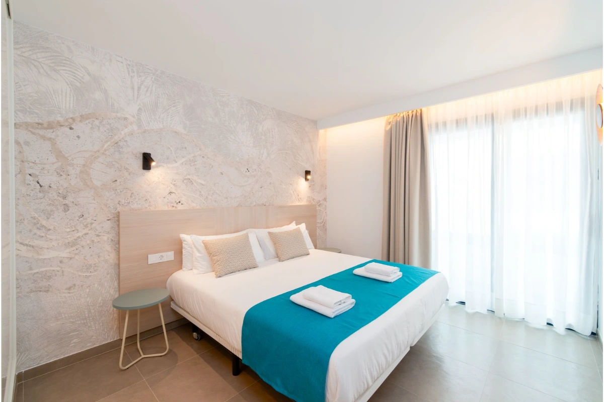 Habitaci&oacute;n moderna con cama doble, cojines y s&aacute;banas azul turquesa.