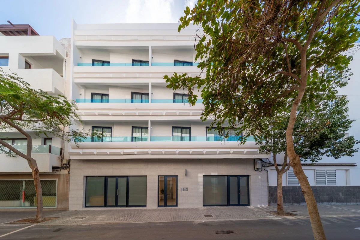 Edificio moderno de tres pisos con balcones y &aacute;rboles al frente.