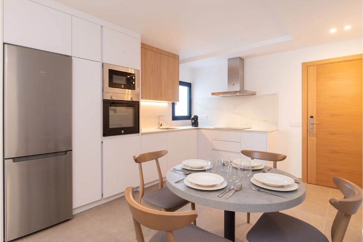 Cocina moderna con mesa redonda y muebles blancos y de madera clara.