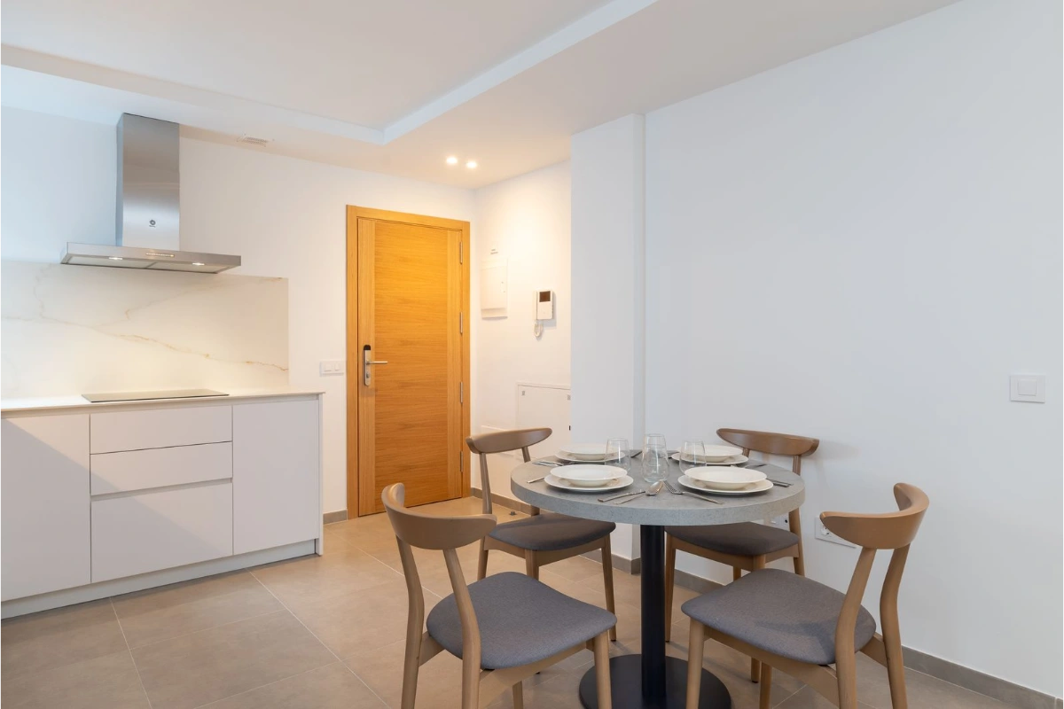 Cocina comedor con mesa redonda, sillas y puerta de madera.