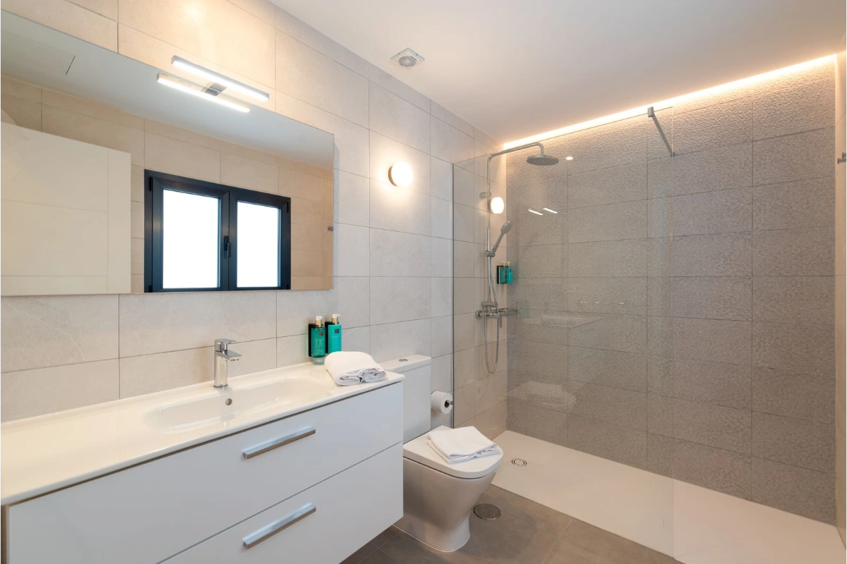 Ba&ntilde;o moderno con ducha, lavabo, espejo y accesorios minimalistas.