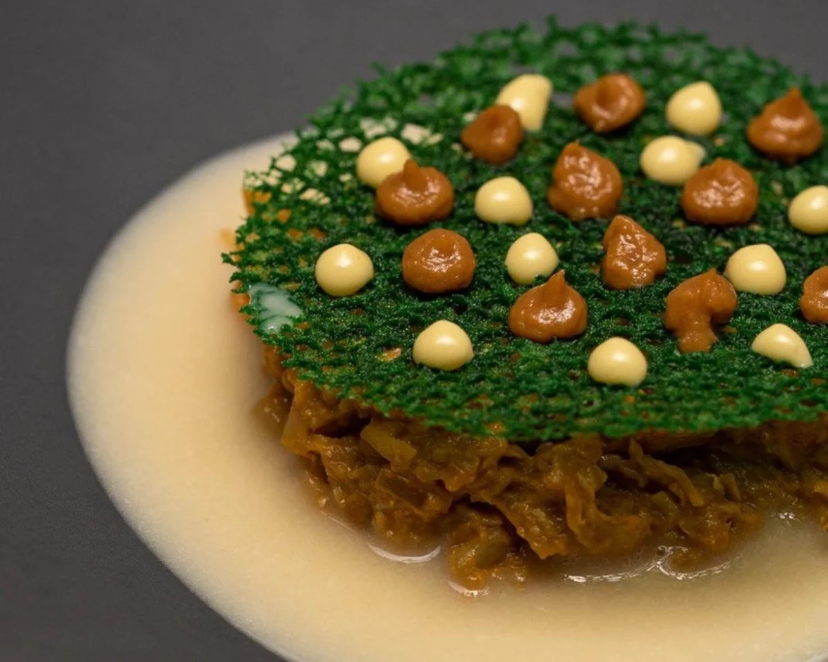 Plato gourmet con crema, carne y una cobertura verde decorada con puntos.