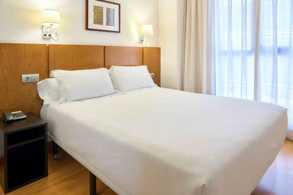 Habitaci&oacute;n de hotel con cama doble y cortinas claras, vista interior